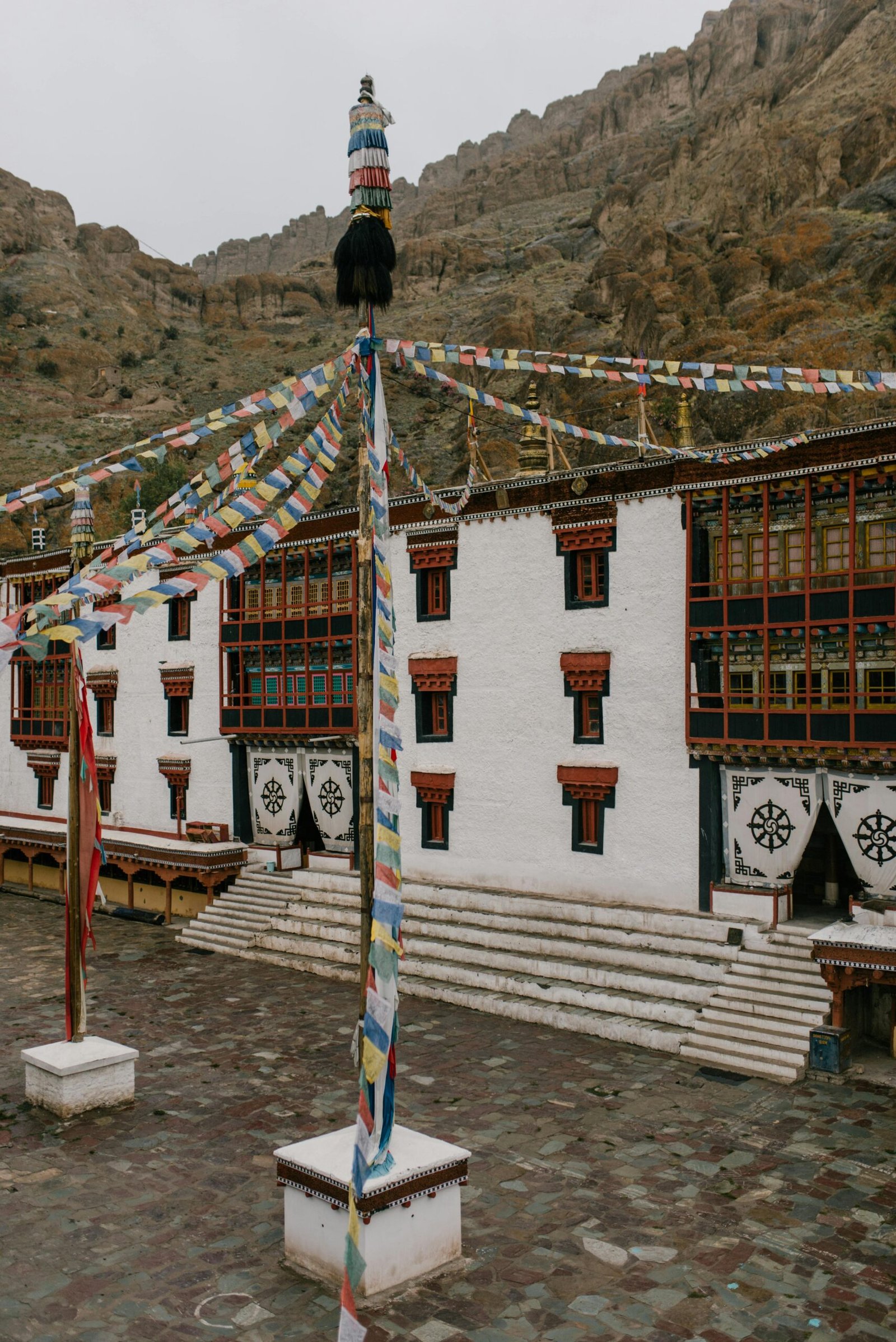 A captivating view of a traditional monastery adorned with colorful prayer flags against a rugged mountainous backdrop.